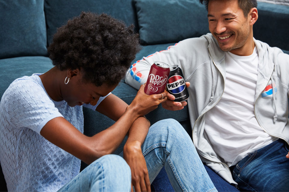 Woman holding Dr. Pepper can and man holding Pepsi can