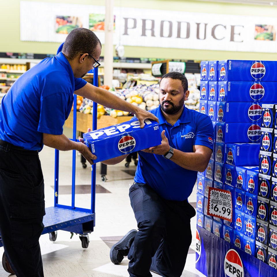 Two employees loading Pepsi cases in a retail store